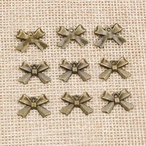 Nine vintage bronze alloy bow pendants neatly arranged on a rustic linen texture background