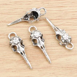 Set of four antique silver bird skull pendants with floral carvings on wood background