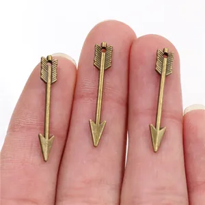Gros plan de trois breloques flèche en bronze 30x5mm sur le doigt pour bijoux DIY
