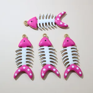 Vista piatta di quattro ciondoli a lisca di pesce in oro con smalto rosa e bianco DIY