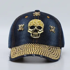 Detailed view of the dark blue denim baseball cap with gold skull and rhinestone brim