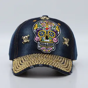 Detail of blue denim baseball cap with rhinestone brim and gold skull embroidery