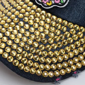 Macro detail of dark denim baseball cap brim with golden rhinestones and floral embroidery