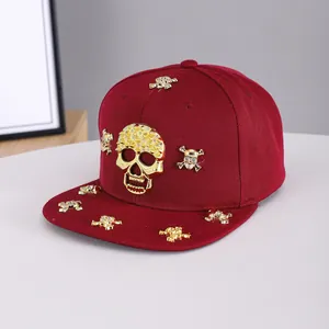 Detail of burgundy snapback hat featuring gold metal skull charms and flat brim hip-hop style