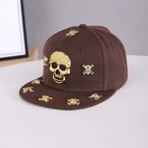 Detail of a brown flat brim hip hop hat with golden metal skull hardware and rhinestone accents