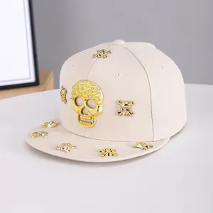 Close-up of golden skull ornaments and rhinestones on a beige flat brim baseball cap