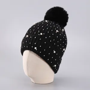 Detail einer schwarzen Strickmütze mit weißen Perlen, Glitzersteinen und Kunstfell-Bommel