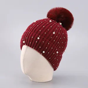Detail der weinroten Strickmütze mit Kunstperlen, Strasssteinen und einem flauschigen Bommel