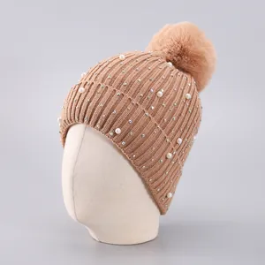 Detail der khakifarbenen Strickmütze mit eleganten Perlen, Strasssteinen und Kunstfellbommel