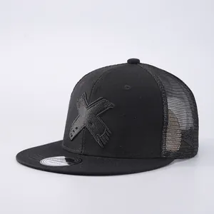 Detailed view of black flat brim trucker hat featuring artistic embroidered X logo and mesh