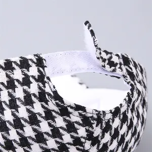 Dettaglio del cinturino in velcro bianco regolabile su un cappello con motivo pied-de-poule