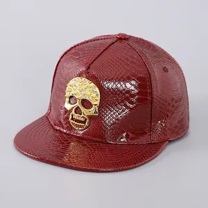 Detail of red faux snakeskin leather snapback cap with golden rhinestone skull ornament