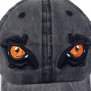 Detail of embroidered orange dragon eyes on dark grey washed cotton baseball cap