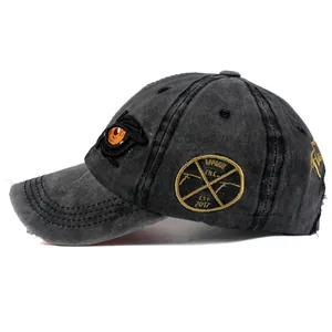 Detail of washed black denim baseball cap with orange eye embroidery and yellow side patch