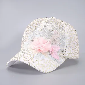 Détail de casquette en maille blanche avec paillettes dorées et grande fleur rose en tissu