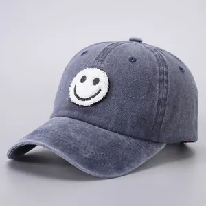 Close-up of a blue denim baseball cap featuring a white fuzzy smiley face patch and texture