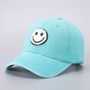 Close-up of a light blue cotton baseball cap with a white embroidered smiley face patch