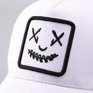 Détail de la casquette blanche montrant la texture en toile et la broderie de visage souriant