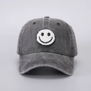 Detail of dark grey washed denim baseball cap with white towel embroidered smiley face