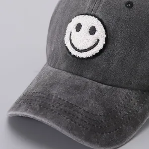 Detailed view of grey washed cotton fabric and embroidered smiley face patch on baseball cap