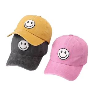 Three washed cotton baseball caps with smiley face patches in yellow, gray and pink