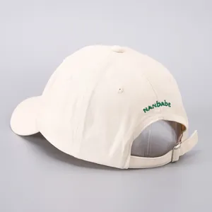 Detail view of beige cotton baseball cap with green NANBABE embroidery and metal buckle