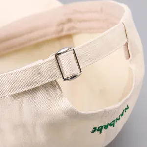 Close-up of adjustable silver buckle and green embroidery on beige cotton baseball cap