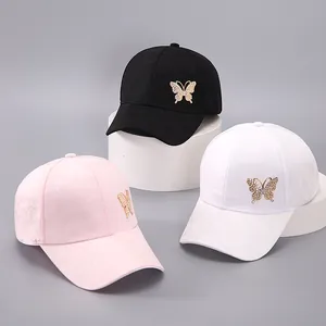 Close-up of baseball caps in black, white, and pink with rhinestone butterfly decorations