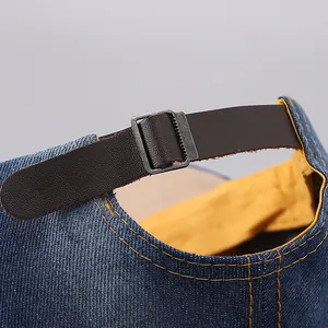 Close-up of the adjustable brown leather strap and metal buckle on a denim baseball cap