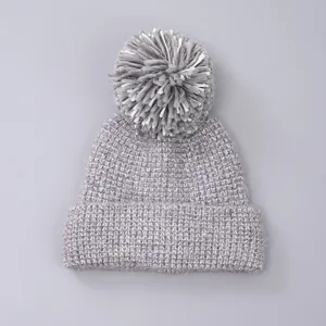 Close-up of thick grey knit winter hat featuring a fluffy mixed-color faux fur pom-pom