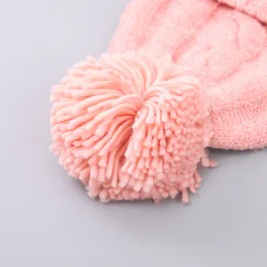 Close-up of pink knitted winter hat featuring a large fluffy faux fur pom-pom detail