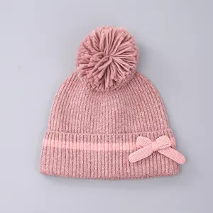 Detail van roze gebreide muts met grote pompon en strik op een effen grijze achtergrond