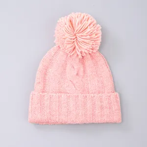 Detailed view of pink cable-knit beanie with large pompom and ribbed windproof cuff