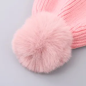 Close-up of pink knitted winter hat featuring a soft faux fur pom-pom and thick texture