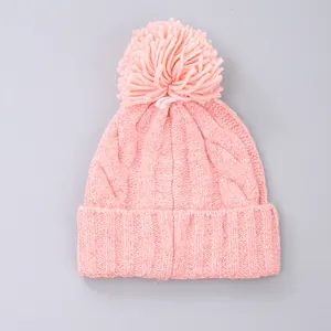 Detailed cable knit pattern on pink winter beanie featuring a soft faux fur pompom decoration