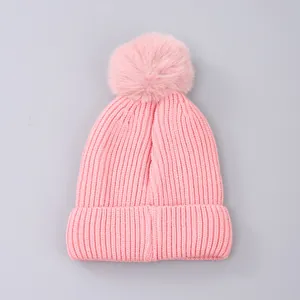 Close-up of pink chunky knit winter hat featuring a fluffy faux fur pom-pom detail