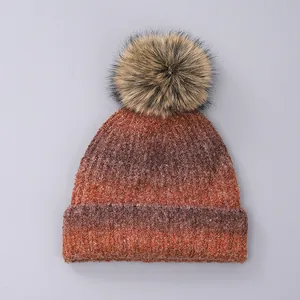 Detail of red-brown gradient knit beanie with fluffy faux fur pompom and ribbed cuff