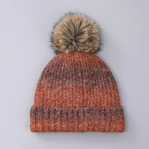 Close-up of knit winter beanie with fluffy faux fur pom-pom and tie-dye texture