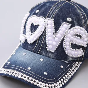 Close-up of denim baseball cap with LOVE embroidery, pearls, and rhinestones on blue fabric