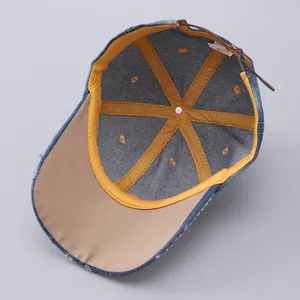 Detail of dark blue denim baseball cap with yellow trim and brown leather strap