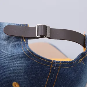 Close-up of blue denim baseball cap back featuring leather strap and metal buckle detail