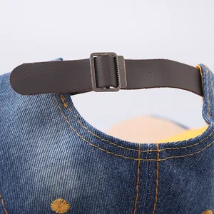 Dettaglio del cinturino in pelle marrone e fibbia in metallo sul cappellino di jeans