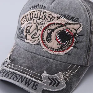 Detailed close-up of vintage washed grey baseball cap with shark embroidery and distressed denim