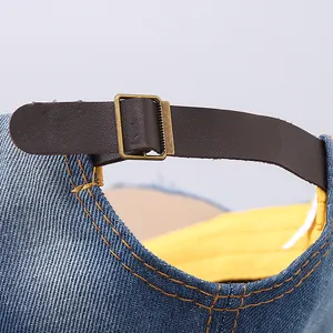 Detail of adjustable brown leather strap and bronze buckle on denim baseball hat