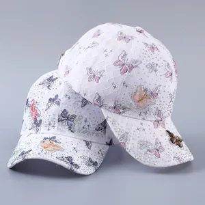Detailed close-up of white lace baseball cap with butterfly prints and rhinestones