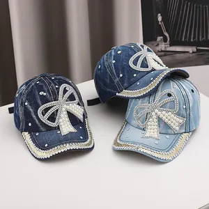 Detailed view of three denim baseball caps featuring pearl and rhinestone bow embellishments
