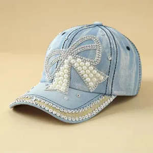 Denim baseball cap with pearl and rhinestone bow decoration shown at a 45-degree angle