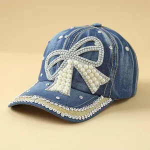 Close-up of denim baseball cap with pearl bow and sparkling rhinestone brim details