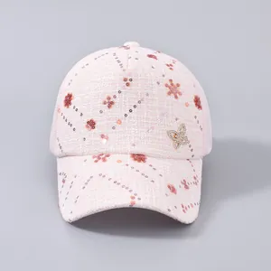 Dettaglio del berretto in tweed rosa con fiori di paillettes e logo a farfalla argento