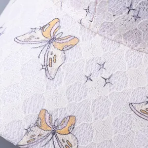 Close-up of white lace fabric with butterfly patterns and star details on baseball cap